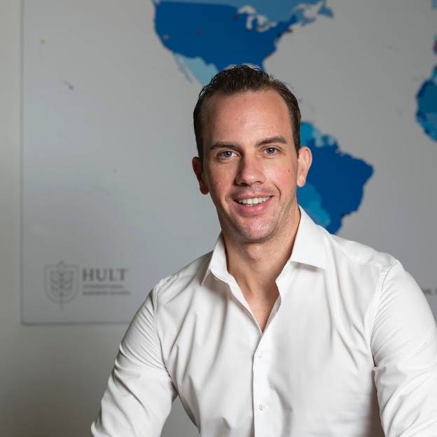 Man in white shirt sits and smiles in front of world map.