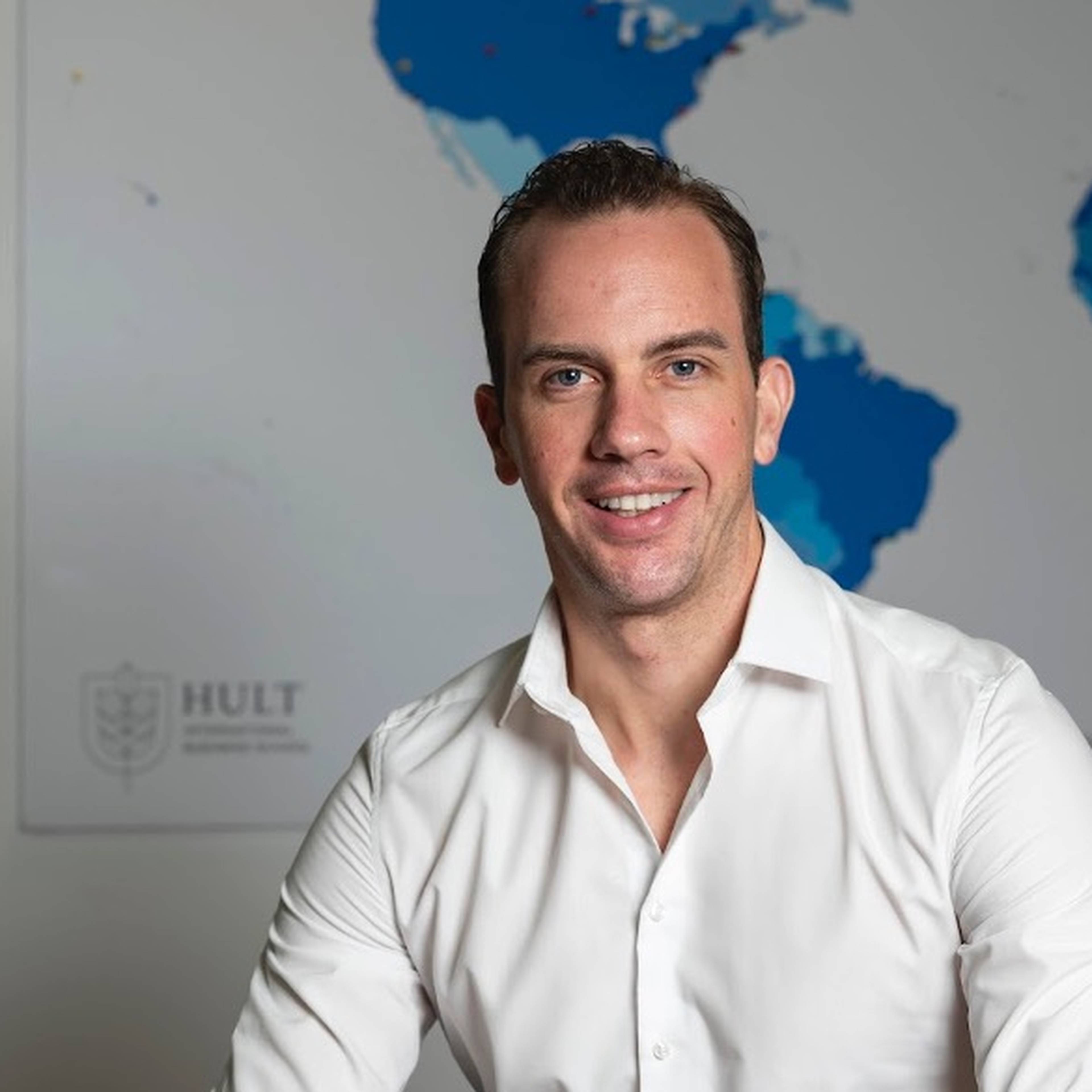Man in white shirt sits and smiles in front of world map.