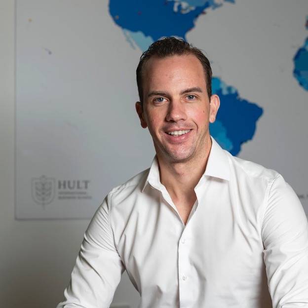 Man in white shirt sits and smiles in front of world map.