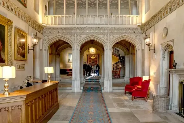 Elegant medieval-style hall with red chairs, arched doorways, and a reception desk.