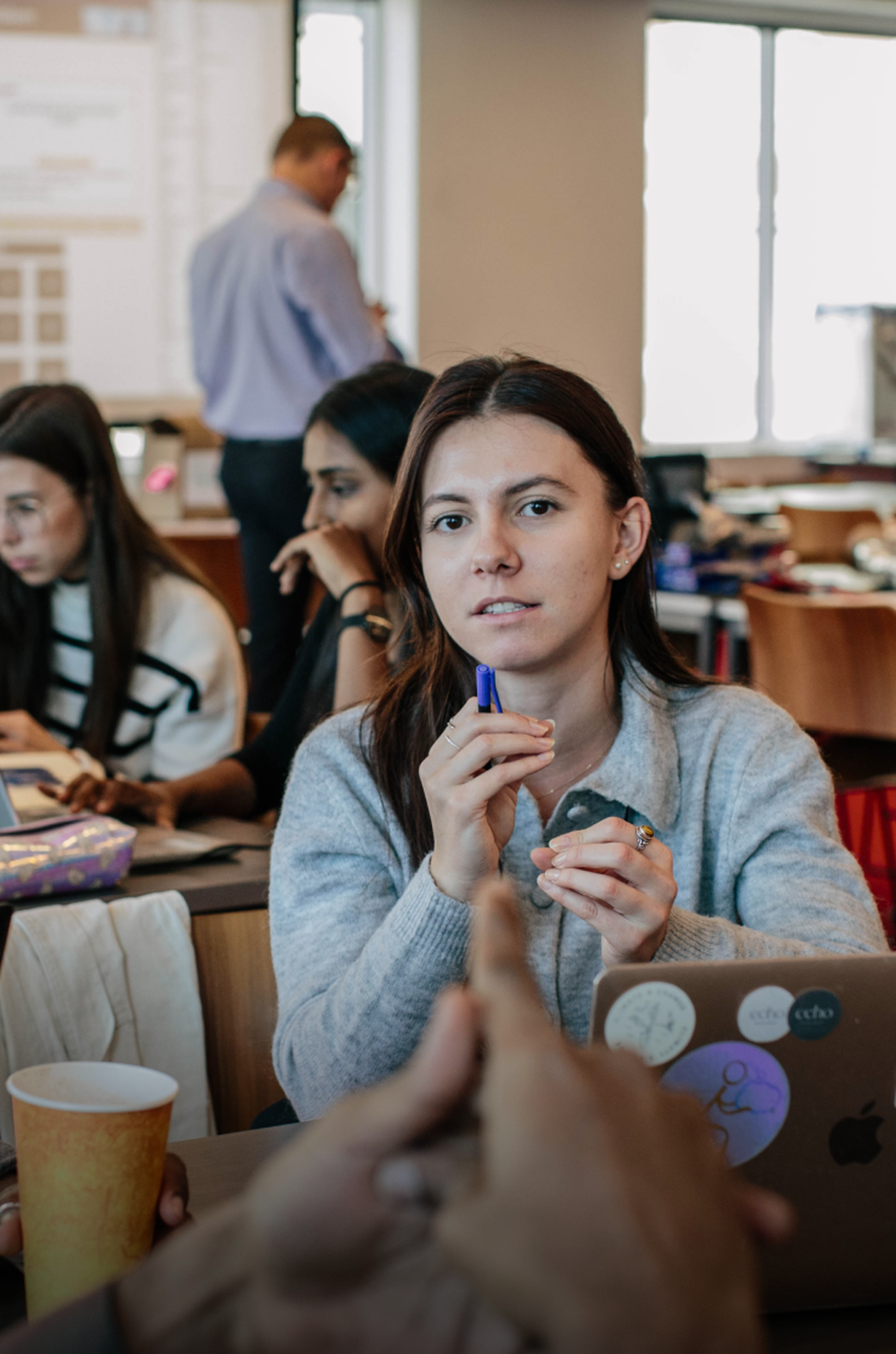 A woman holding a pen listens attentively in a classroom setting.