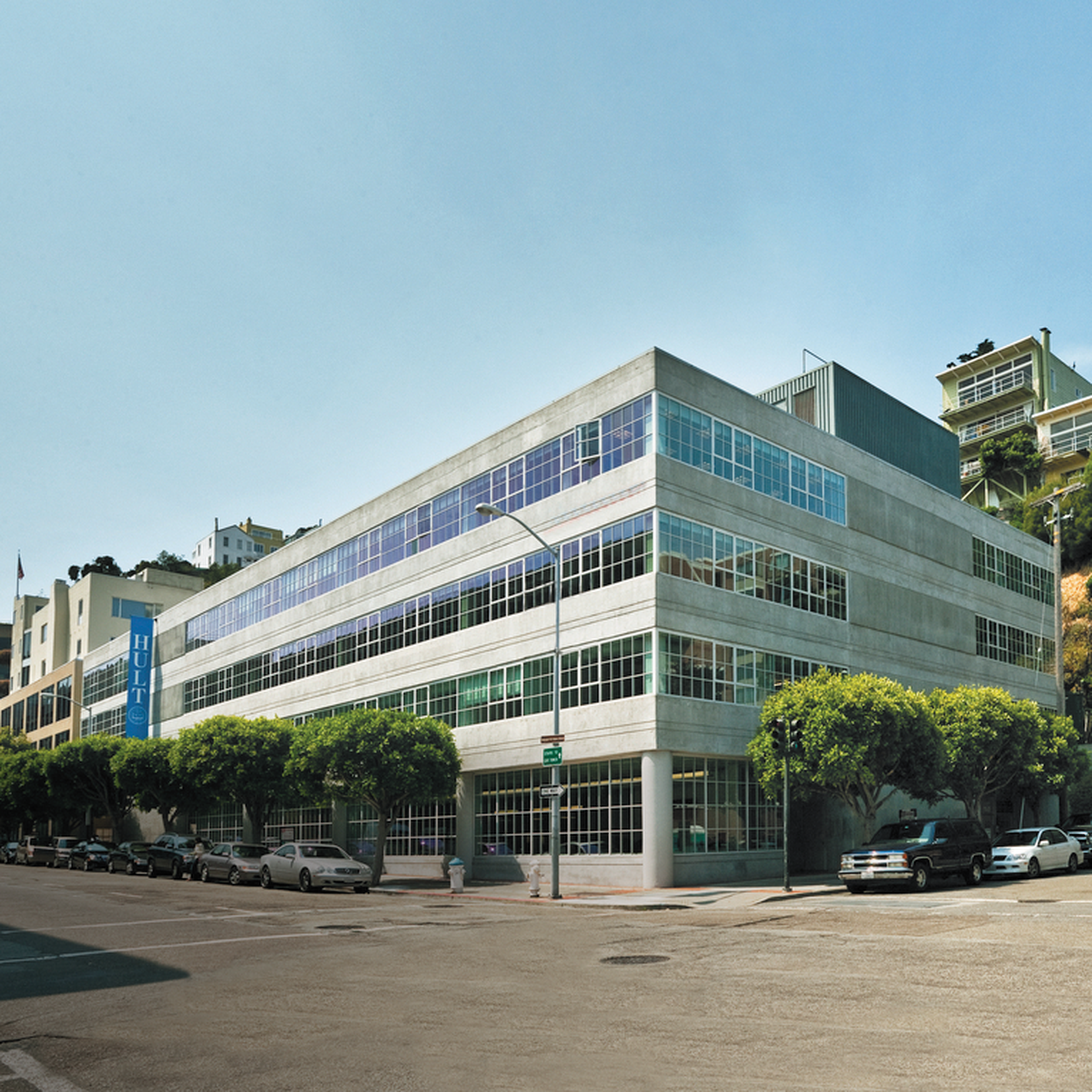 A modern, multi-story building with large windows on a sunny street corner.