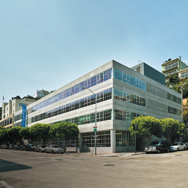 A modern, multi-story building with large windows on a sunny street corner.