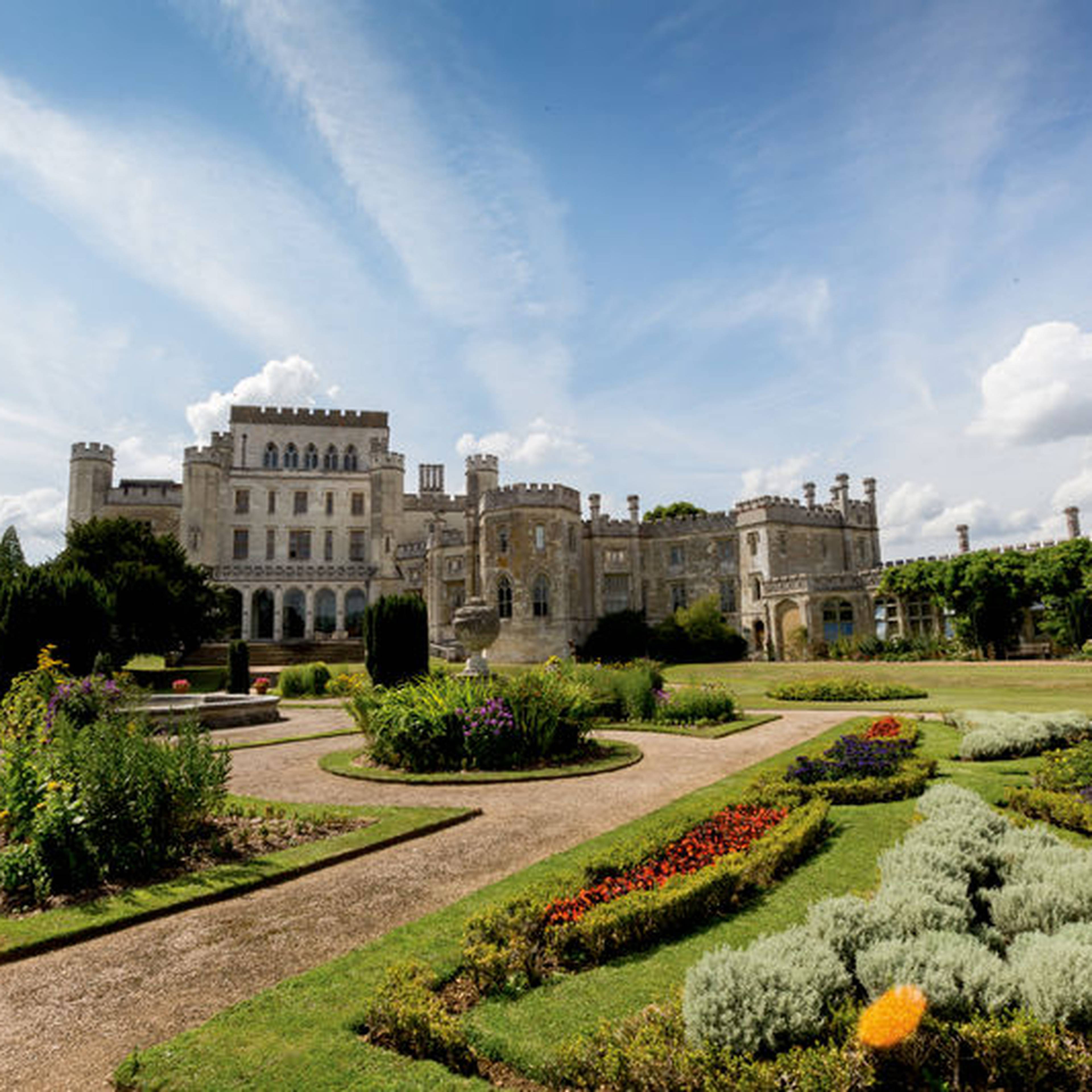 A grand castle with towers and gardens under a blue sky with scattered clouds.