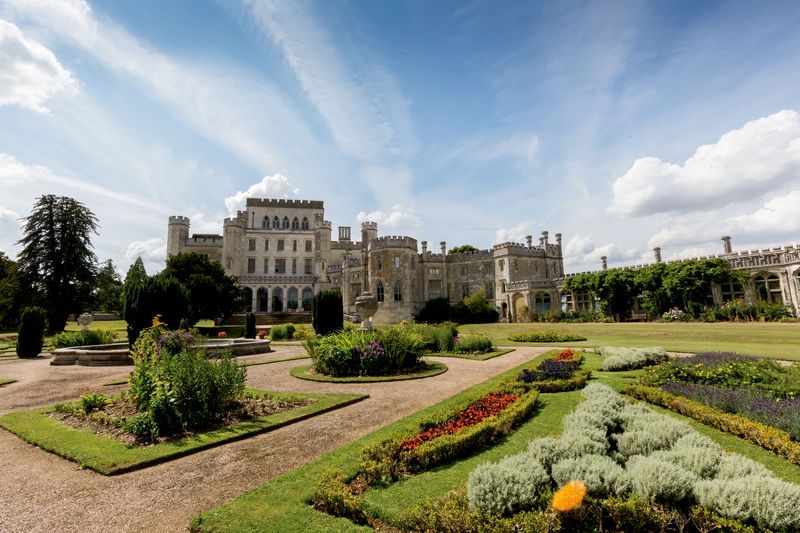 A grand castle with towers and gardens under a blue sky with scattered clouds.