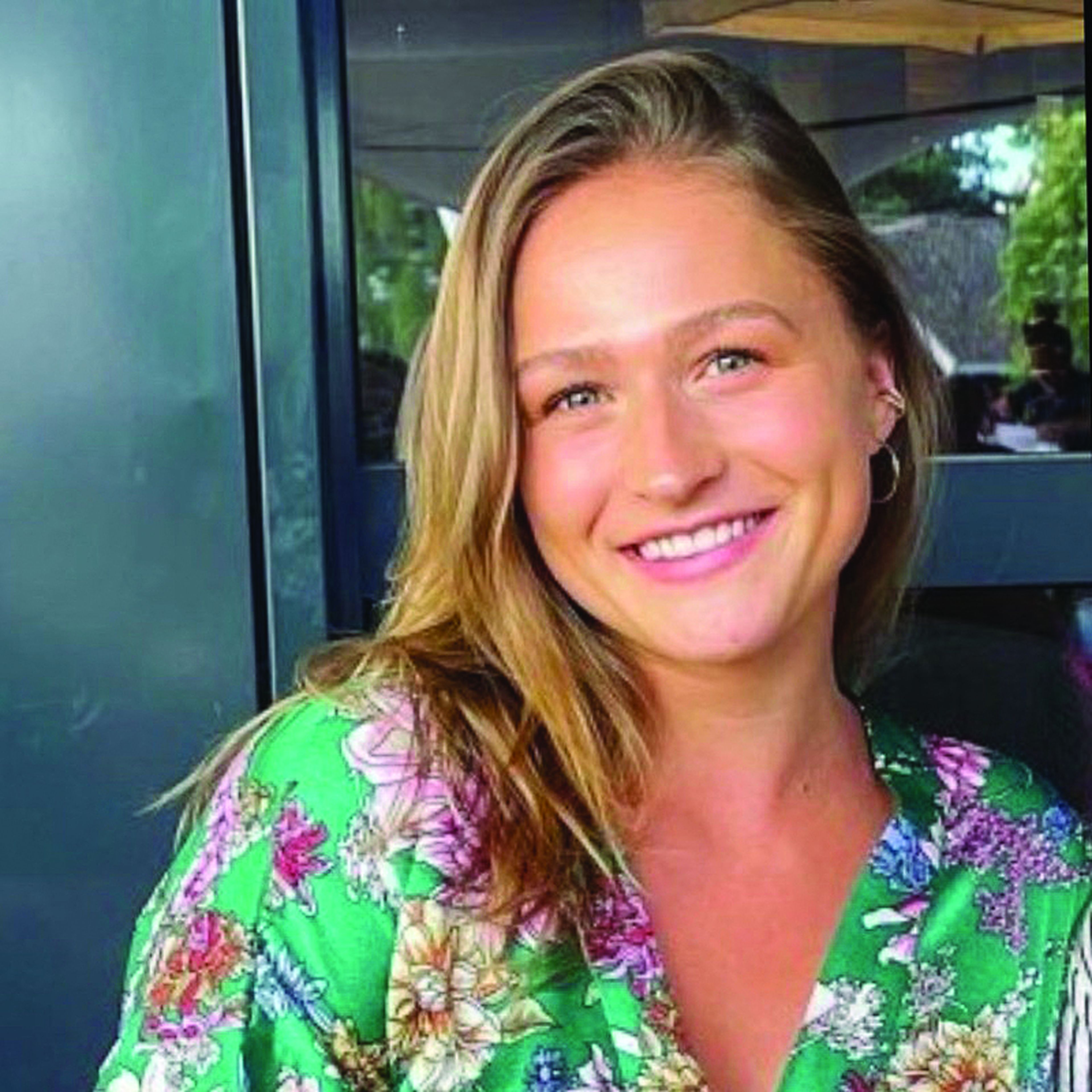 Smiling person in floral clothing sitting outdoors.