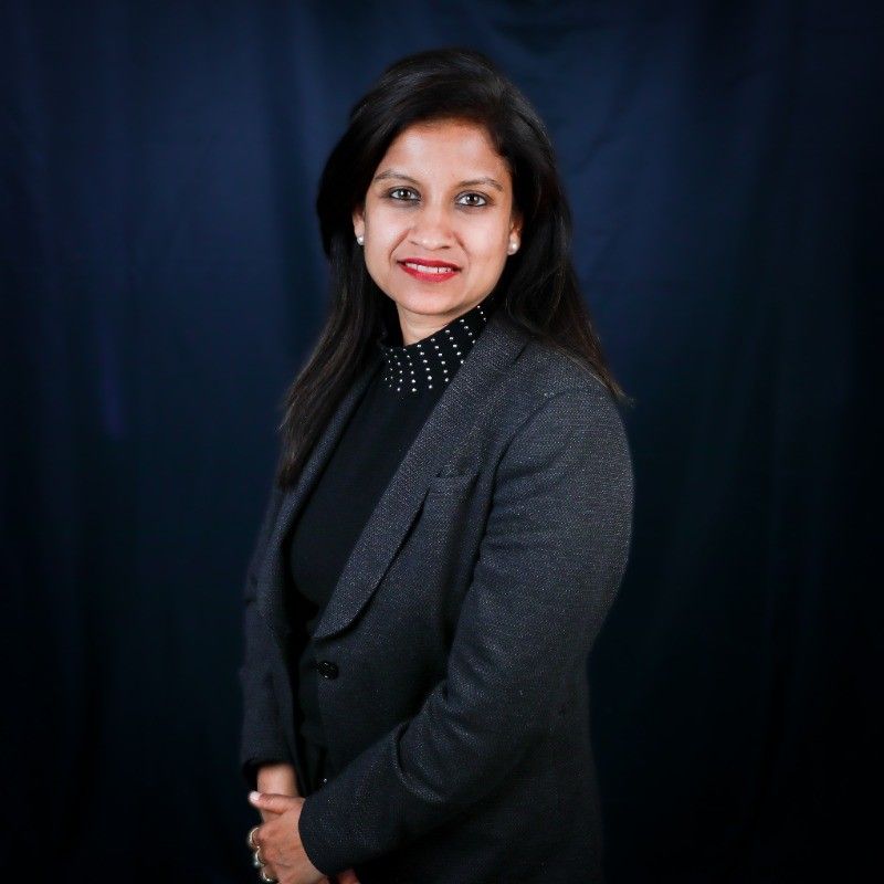 A woman in a grey suit smiles against a dark blue background.