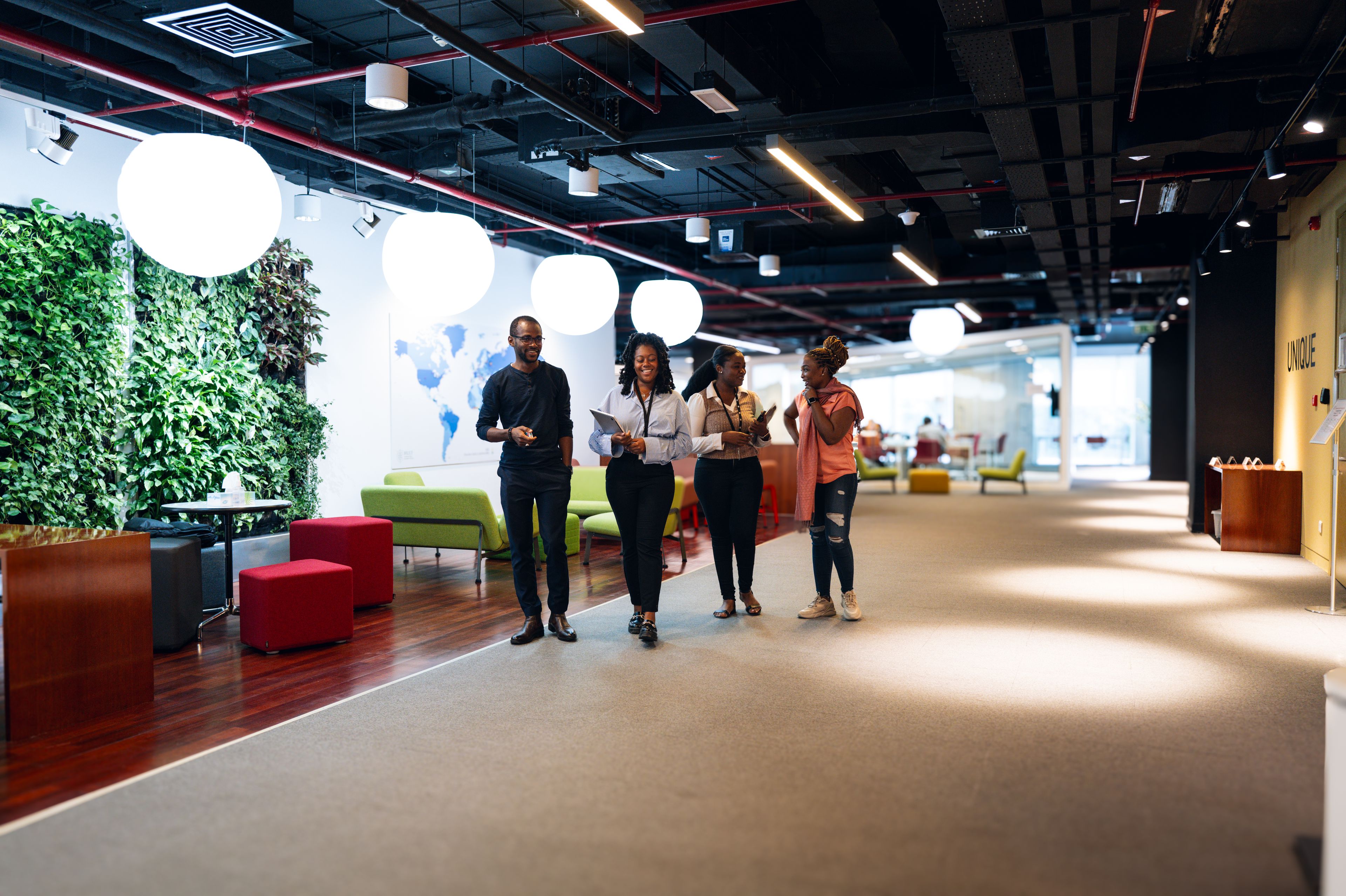 Group of four people walking and talking in a modern office hallway.