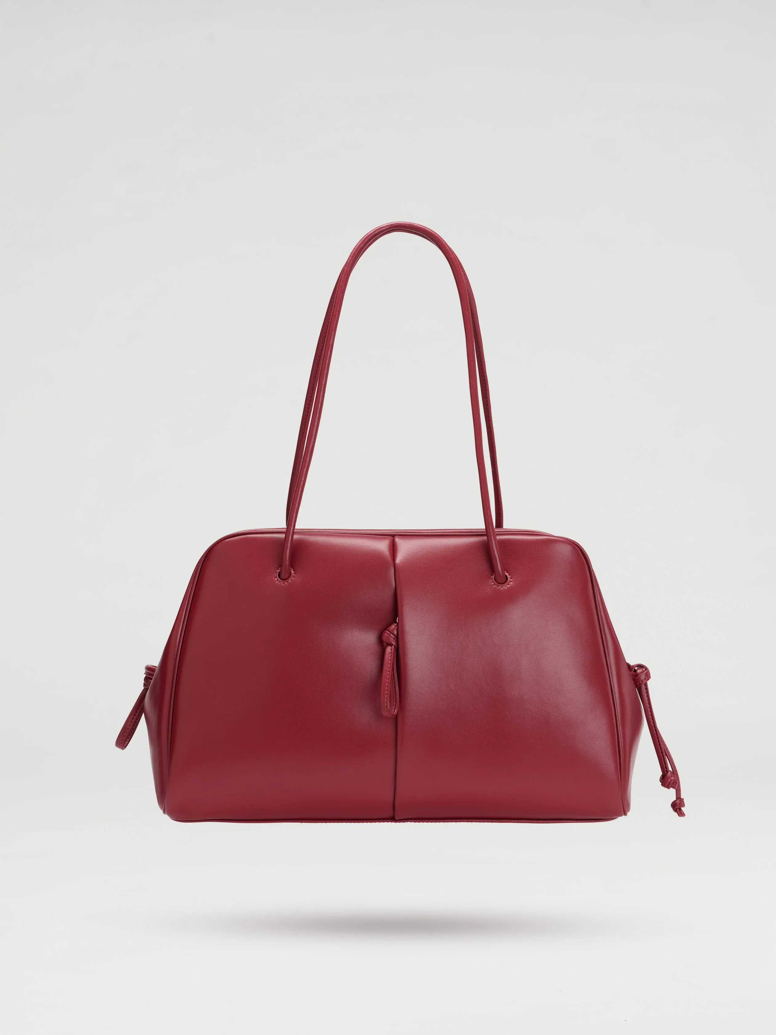 A red leather handbag with two long handles and a smooth, minimalist design, set against a plain white background.