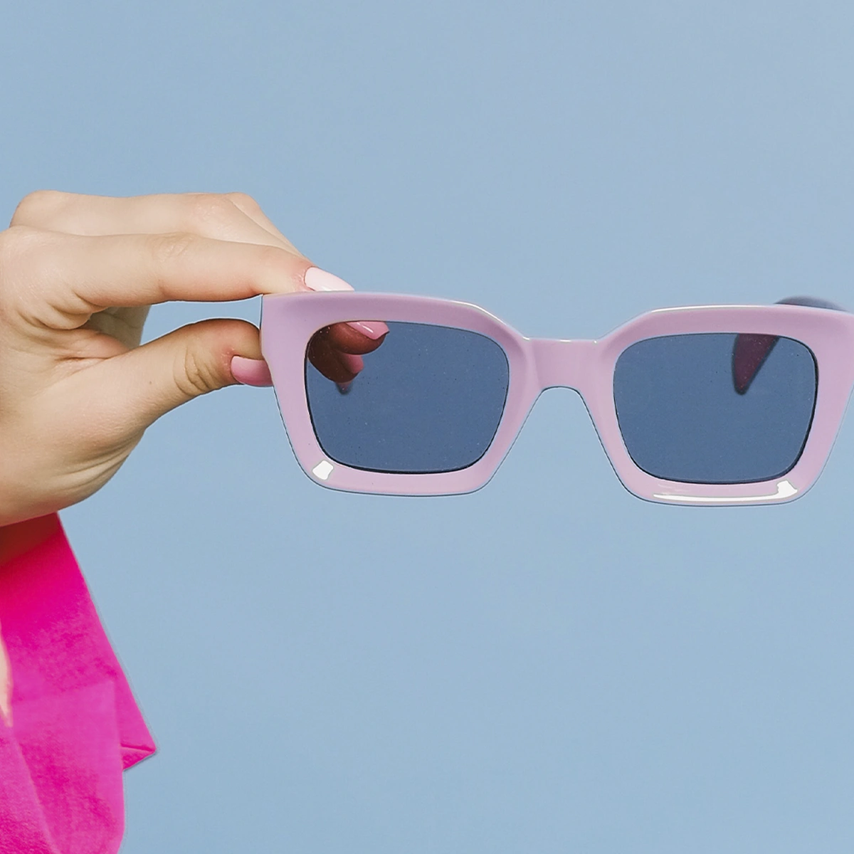 Roze zonnebril in uitgestrekte  hand met blauwe achtergrond