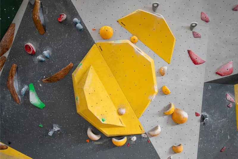 Yellow geometric climbing holds on an indoor wall with various other colorful holds on a speckled gray surface.