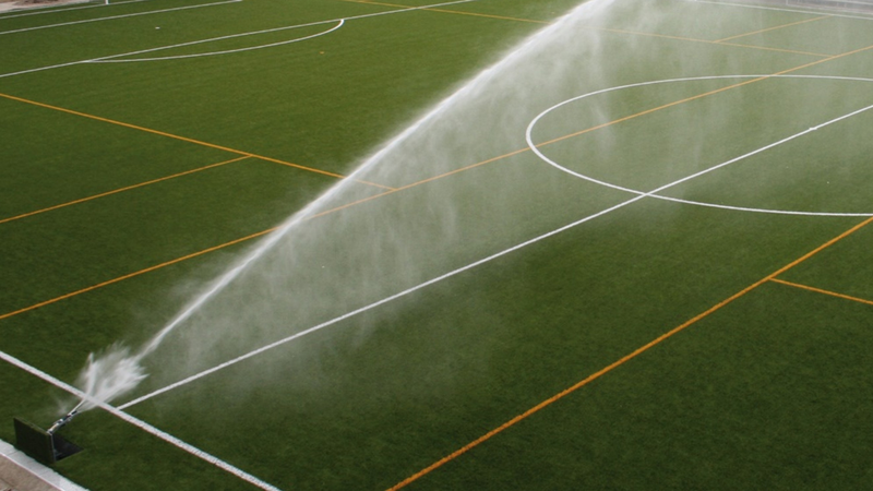 Close view of sprinkler applying water evenly on a sports field in light wind