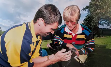 Alison pictured with Roy Keane as they both pet a small black dog outdoors on a grassy field.