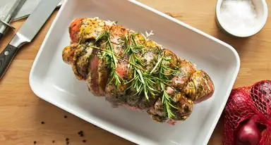 A perfectly seared beef tenderloin steak garnished with fresh rosemary sprigs is plated on a white rectangular dish, accompanied by a knife, salt, and festive holiday decorations o