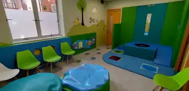 A bright, colorful playroom for young children featuring blue and green furniture, interactive play equipment, comfortable seating areas, and educational wall decorations.