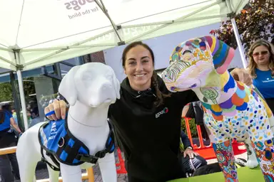 A smiling woman posing next to a colorfully painted sculpture and a white dolphin statue.