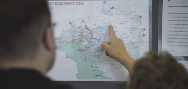 Eine Person deutet auf eine Karte, über der "Klimapakt 2035" steht.