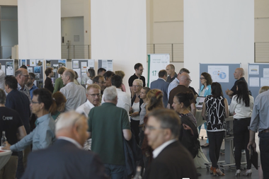 Menschen tauschen sich in einem Foyer aus, im Hintergrund Stellwände mit angepinnten Materialien.