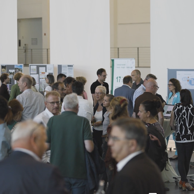 Menschen tauschen sich in einem Foyer aus, im Hintergrund Stellwände mit angepinnten Materialien.