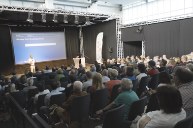 Blick vom Publikum aus auf eine Bühne, hinter dem Vortragenden steht "günster Strom für günstige Wärme" auf der Folie.