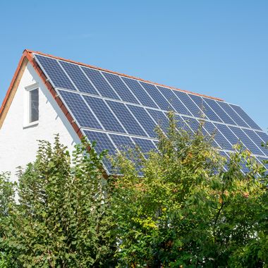 Solarpaneele auf einem Einfamilienhaus, grüne Bäume im Vordergrund.