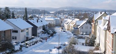Blick in eine Straße mit Wohnhäusern, alles ist weiß mit Schnee bedeckt.