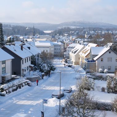 Blick in eine Straße mit Wohnhäusern, alles ist weiß mit Schnee bedeckt.