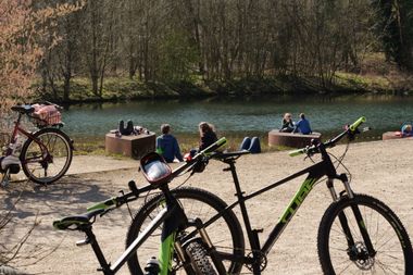 Fahrräder stehen im Vordergrund, dahinter Menschen an einem Fluss.