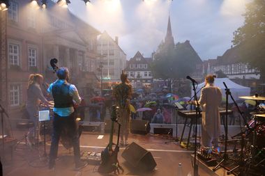 Blick von einer Bühne auf die Band und das Publikum auf einem großen Platz in der Stadt.