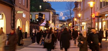 Menschen in einer Einkaufsstraße in Detmold die weihnachtlich geschmückt ist, über der Gasse prangt der beleuchtete Schriftzug "Weihnachtsmarkt".