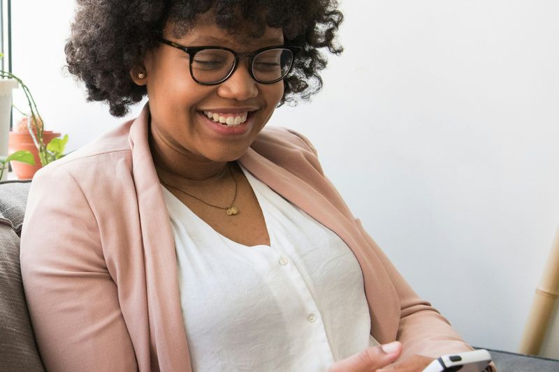 A woman smiling at her phone on a sofa