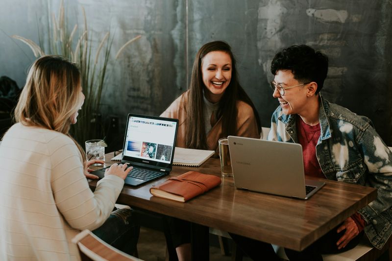 Three colleagues laughing together while working on laptops