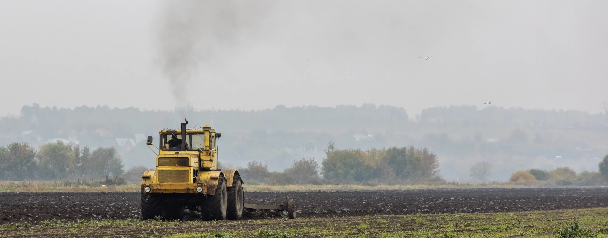 grim yellow tractor plows field after harvest before winter cloudy foggy autumn morning