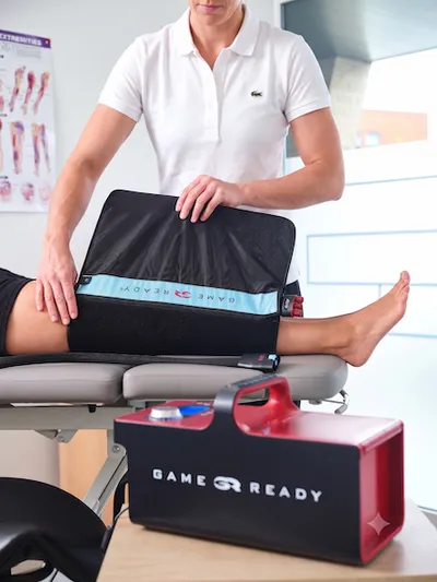 A woman physical therapist in wrapping a Game Ready sleeve around the knee of a patient.