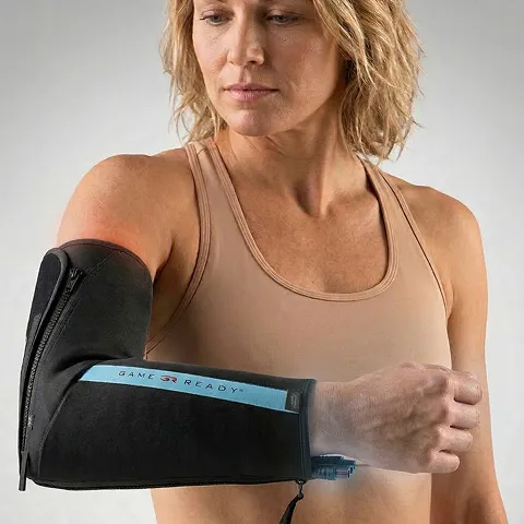 A person wears a cold compression therapy wrap on their elbow, designed for recovery, with a visible brand name.