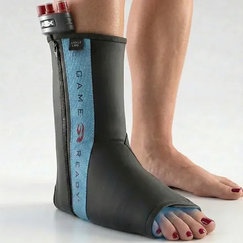 A person wearing a black and blue therapeutic ankle wrap with Game Ready branding, featuring exposed toes and attached tubes at the top.