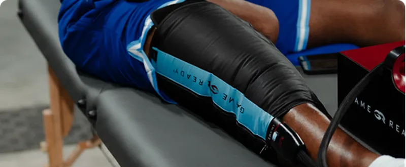 An athlete's leg on a table with a black and blue Game Ready compression wrap.
