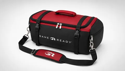 Closed red and black Game Ready carry bag with zip compartments, carry handle, and padded adjustable shoulder strap.