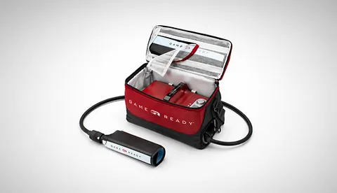 Open red and black Game Ready carry bag showing the control unit stored inside, with a connector cable and battery pack beside it.