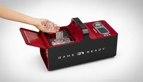 A Game Ready machine with the reservoir open and a hand adding ice cubes.