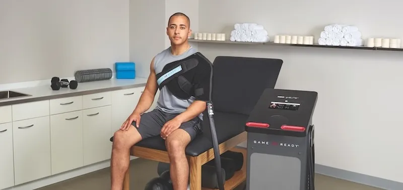 A person sits on a therapy bench using a Med4Elite, surrounded by fitness equipment and towels in a clinical setting.