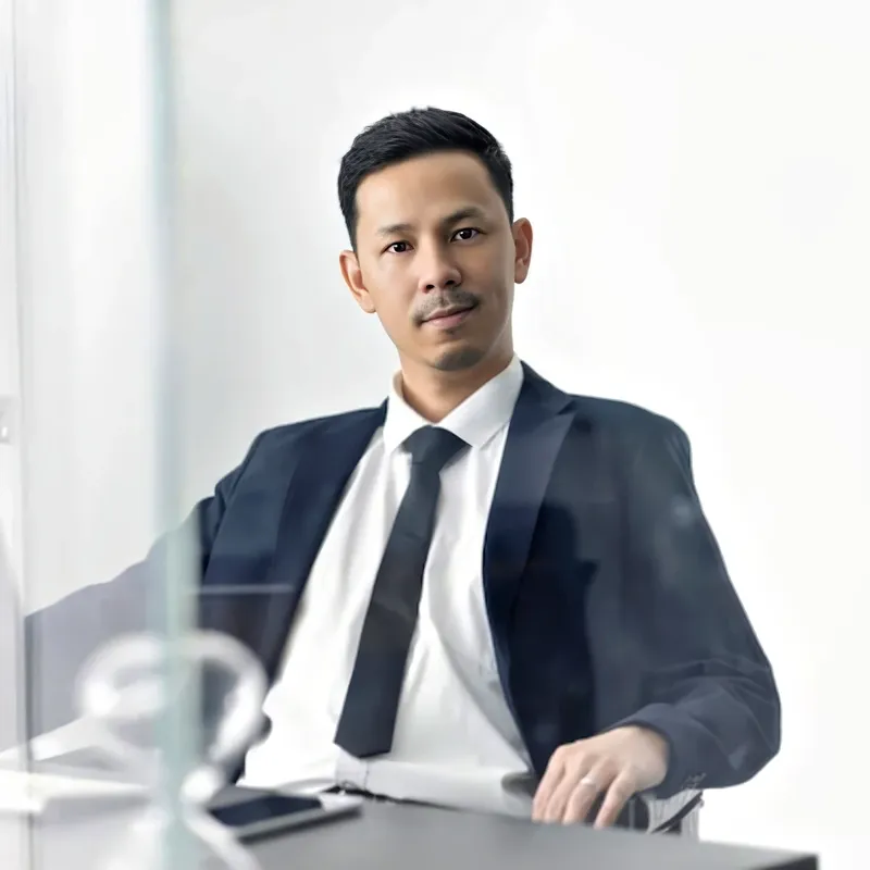 Lawyer in formal navy suit with tie at a desk, indoor architectural backdrop, representing the Litigator attire register