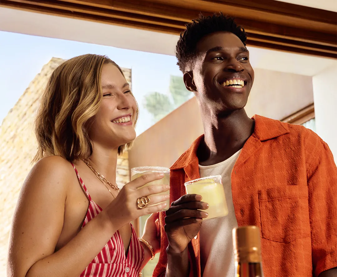 Cointreau cocktails with lime held by two people on sunny terrace with bottle and fresh citrus