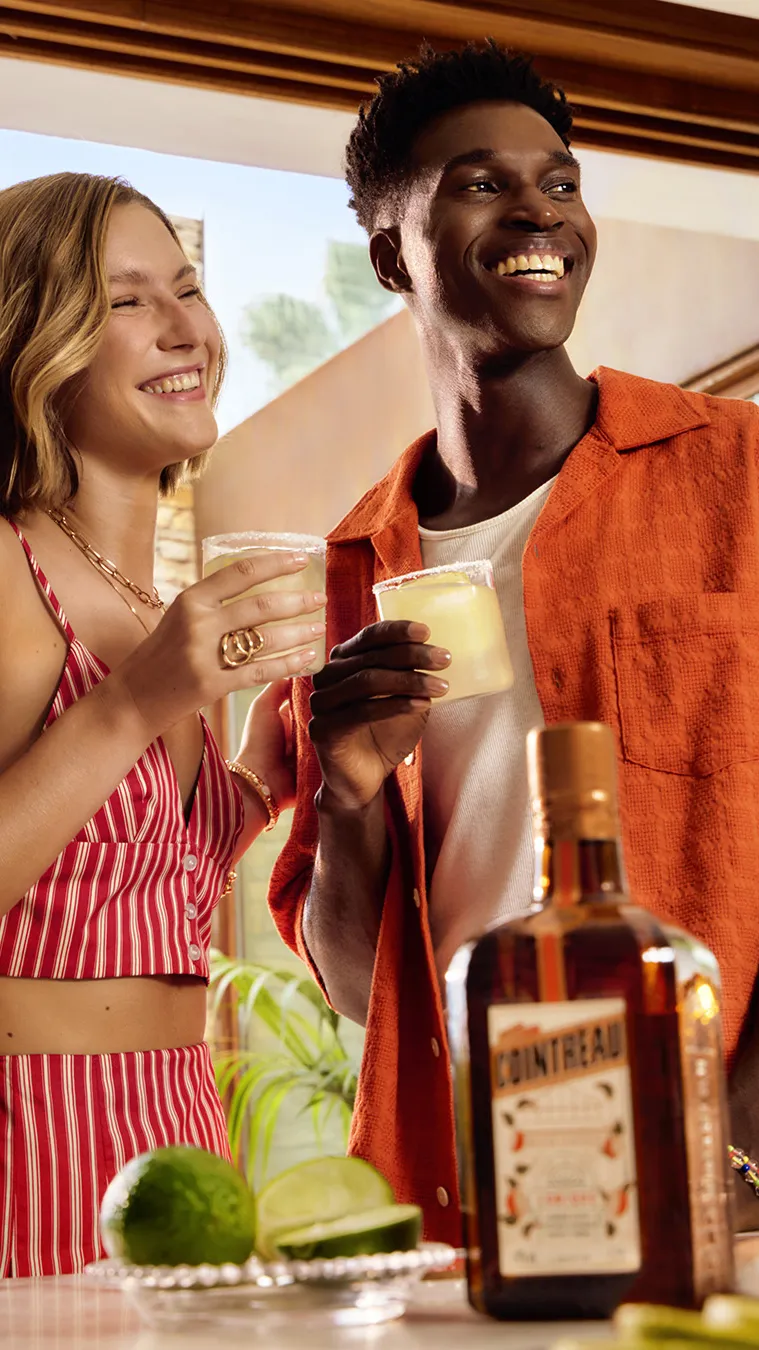 Cointreau cocktails with lime held by two people on sunny terrace with bottle and fresh citrus