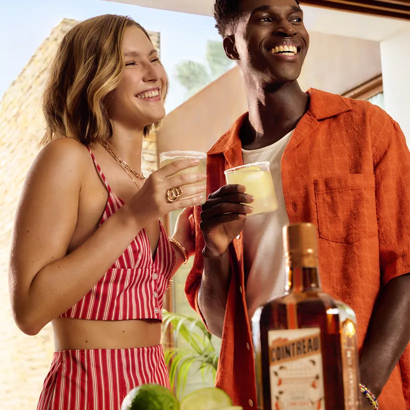 Cointreau cocktails with lime held by two people on sunny terrace with bottle and fresh citrus