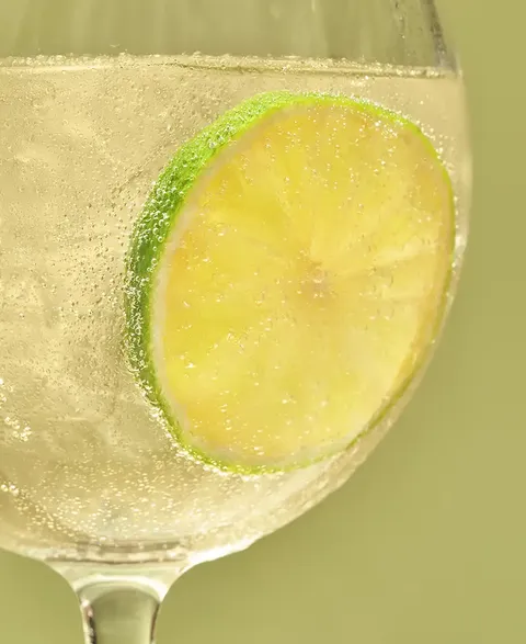 A close-up of a glass filled with Cointreau Citrus Spritz Lemon & Lime in front of a green background
