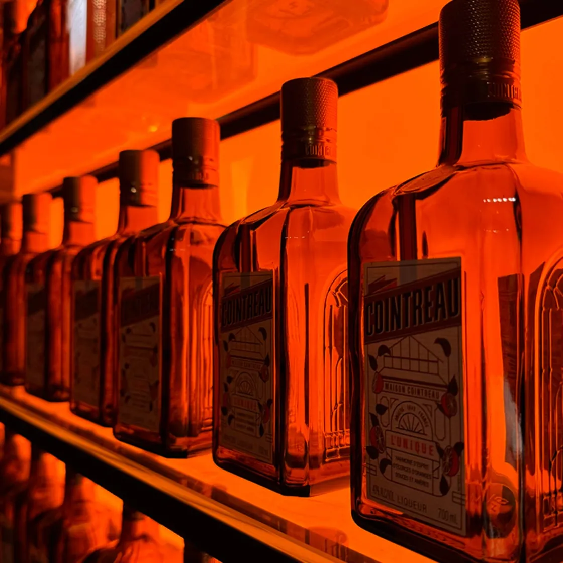 Bottles of Cointreau orange liqueur lined up on a shelf with orange colored lighting