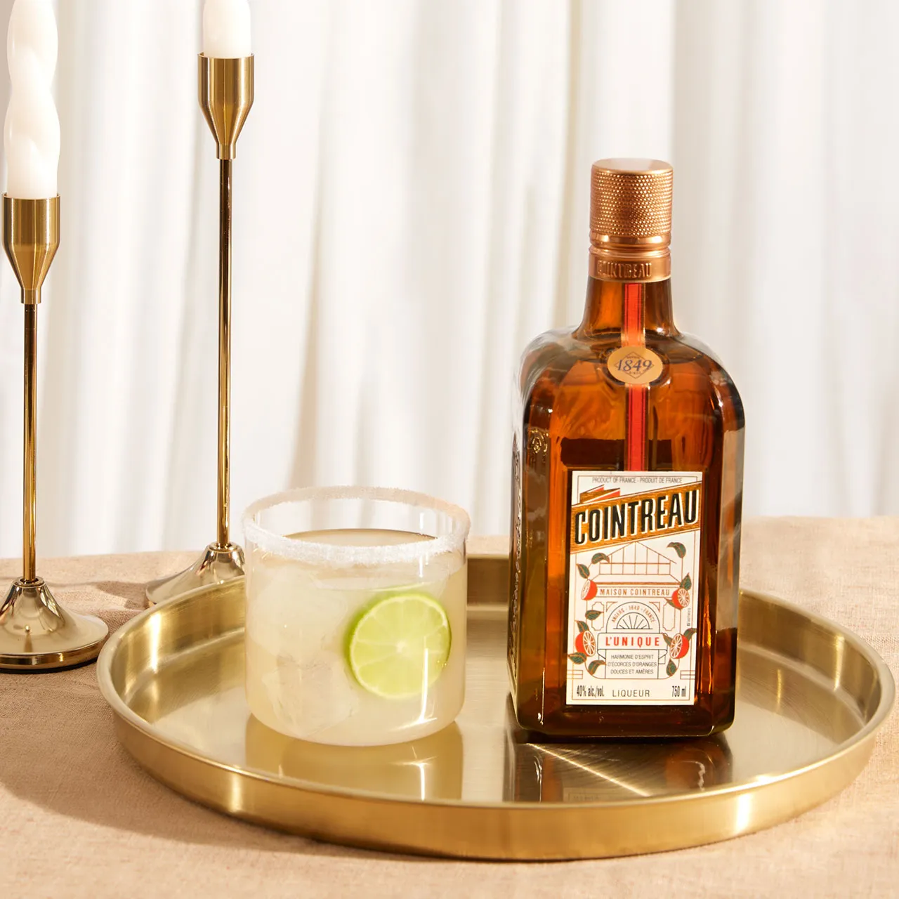 A bottle of Cointreau and a tumbler with a pale yellow cocktail served on a golden tray