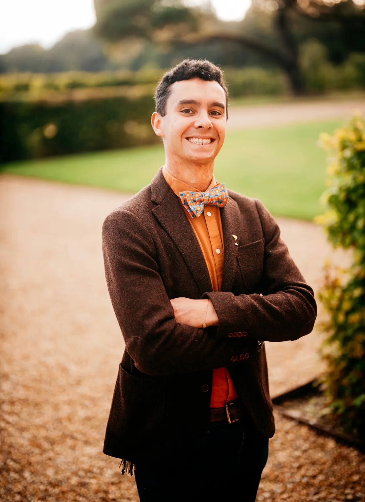 A medium shot of Alfred Cointreau in brown blazer with colourful bow tie standing in garden