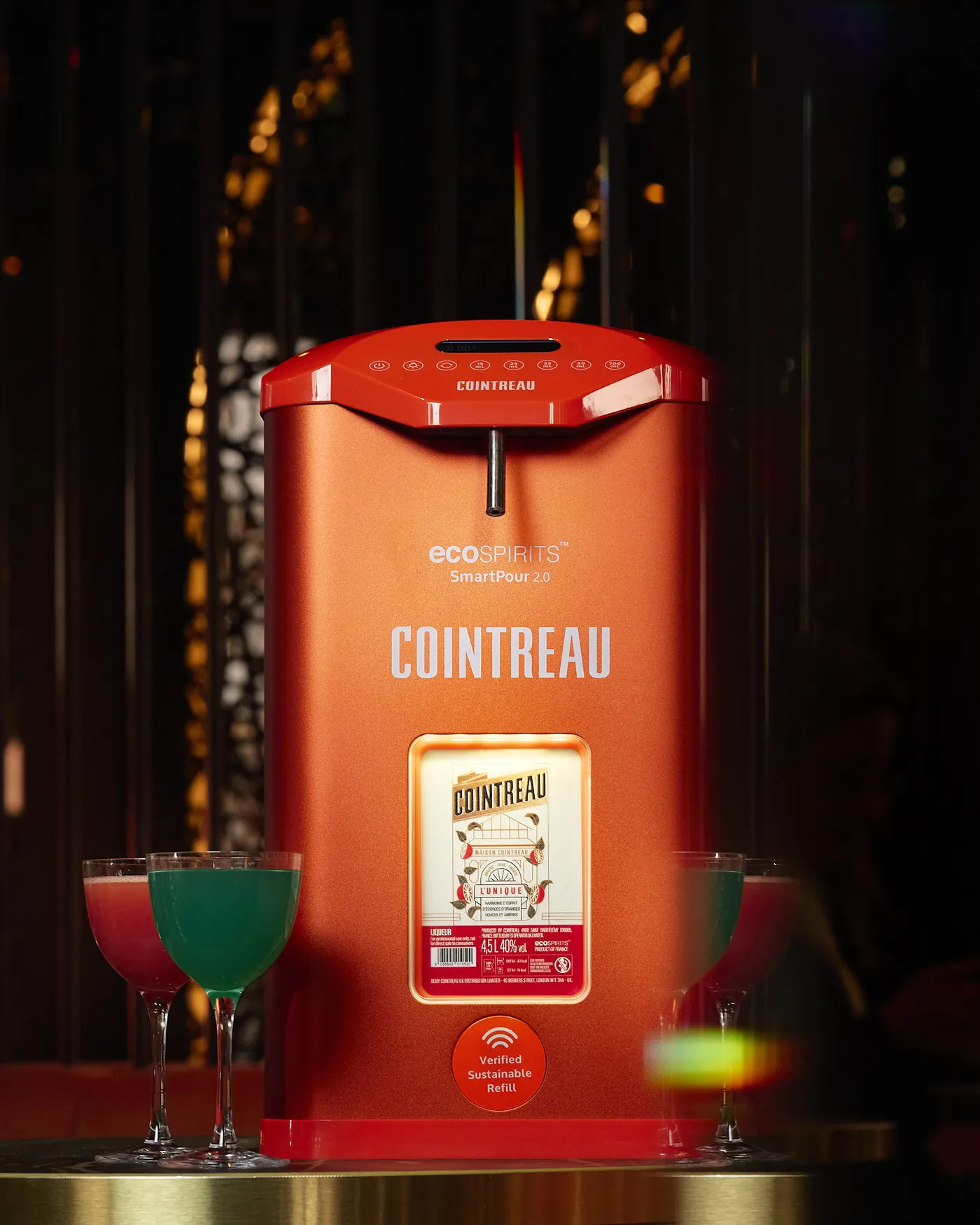 Cointreau SmartPour 2.0 refill station surrounded by colorful cocktails on a bar counter, highlighting a sustainable refill system.